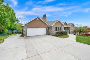 View of front of property featuring stone siding, concrete driveway, a garage, stucco siding, and a chimney