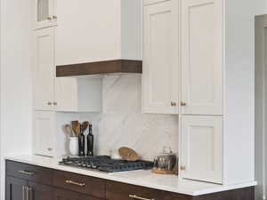 Two tone kitchen featuring dual tone cabinets, backsplash, stainless steel gas stovetop, and light stone counters