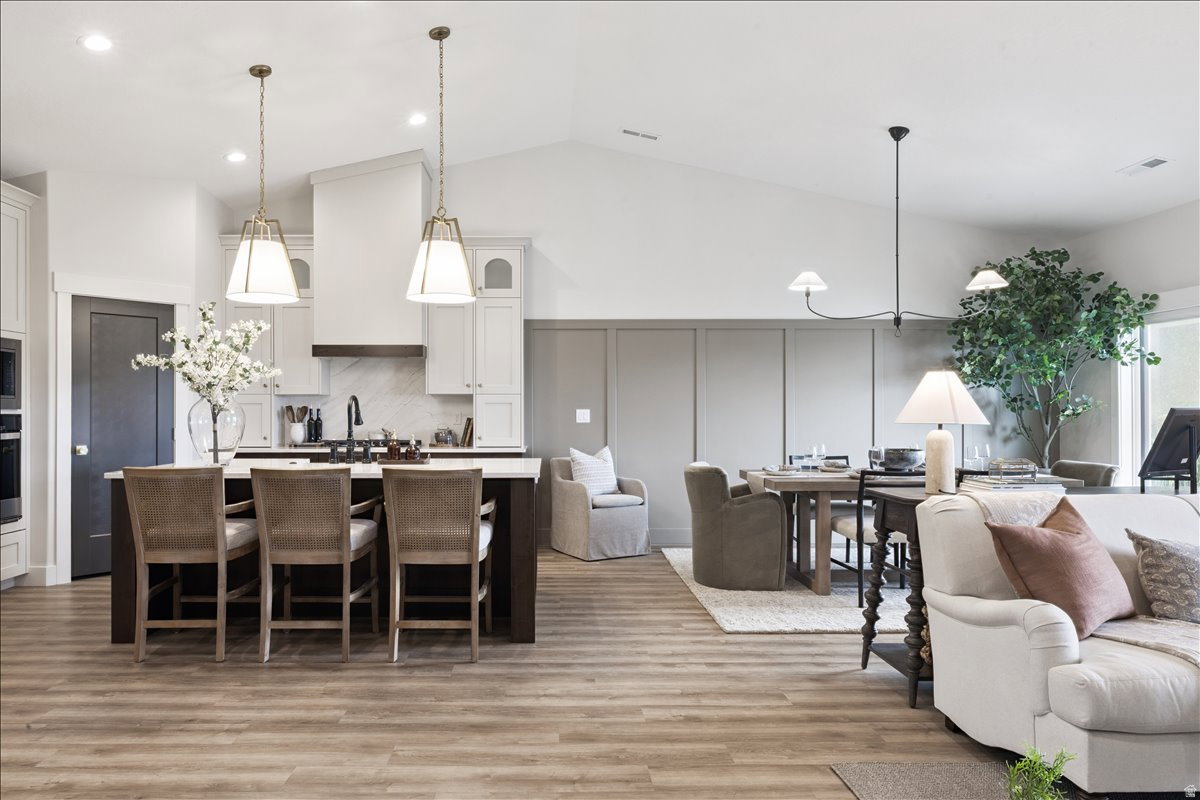 Dual tone kitchen featuring open floor plan, a breakfast bar, a kitchen island with sink, light wood-type flooring, and vaulted ceiling