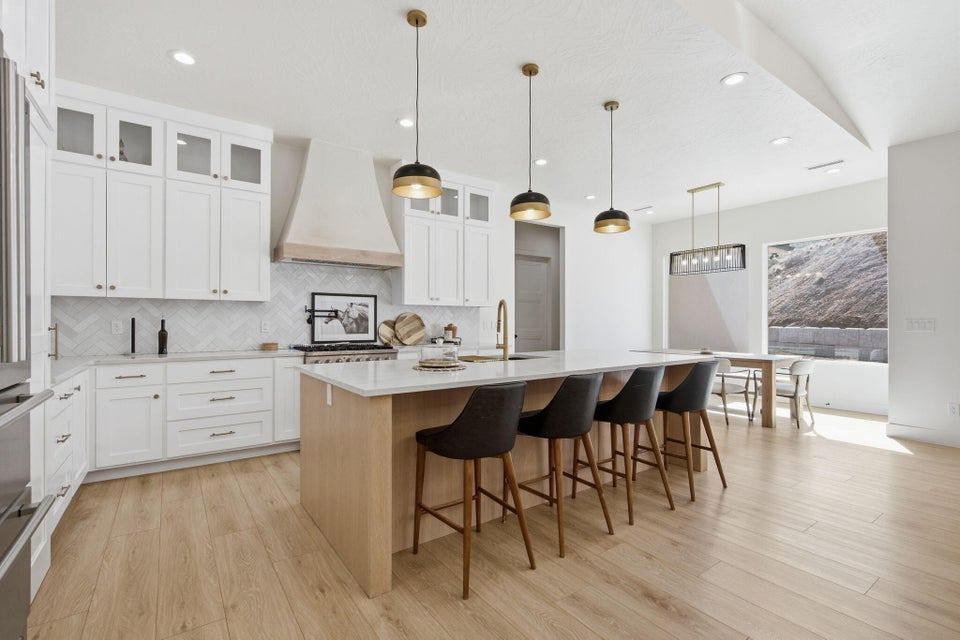 Two tone kitchen featuring pendant lighting, a center island with sink, light stone countertops, light wood finished floors, and a kitchen bar