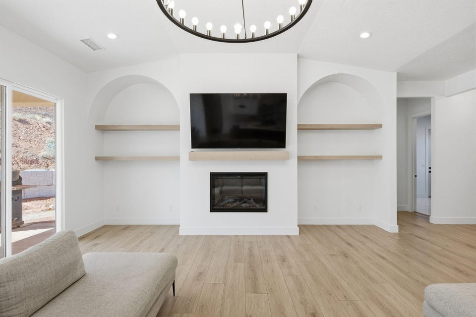 Living area featuring built in shelves, light wood-type flooring, a glass covered fireplace, and recessed lighting