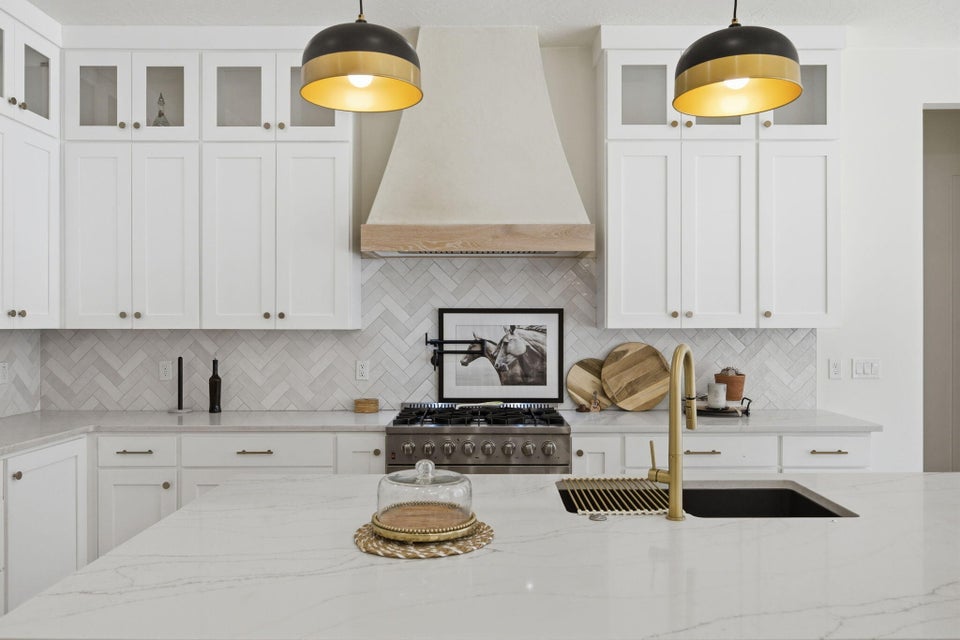 Kitchen with glass fronted cabinets, white cabinets, and light stone counters