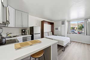 Kitchen with light countertops, a breakfast bar area, freestanding refrigerator, gray cabinetry, and light wood finished floors