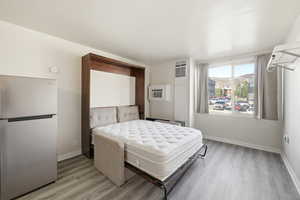 Bedroom featuring freestanding refrigerator, light wood-type flooring, and a heating unit