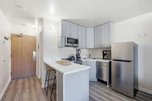 Kitchen featuring light countertops, stainless steel appliances, a breakfast bar, light wood-type flooring, and a peninsula