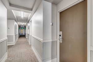 Corridor featuring light colored carpet and a wainscoted wall
