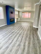 Unfurnished living room with crown molding, a large fireplace, light wood-type flooring, and a textured ceiling