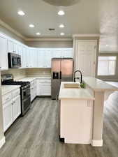Kitchen with an island with sink, stainless steel appliances, light countertops, white cabinetry, and crown molding