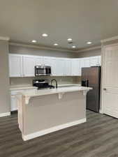 Kitchen featuring a kitchen bar, white cabinets, stainless steel appliances, a center island with sink, and crown molding