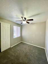 Unfurnished bedroom with dark carpet, a textured ceiling, a closet, and a ceiling fan