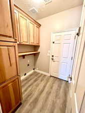 Laundry room with cabinet space, light wood-style floors, hookup for an electric dryer, and a textured ceiling