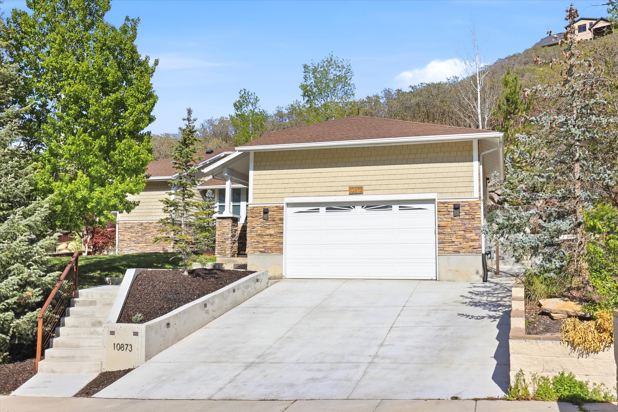 View of front facade with driveway, stone siding, and an attached garage