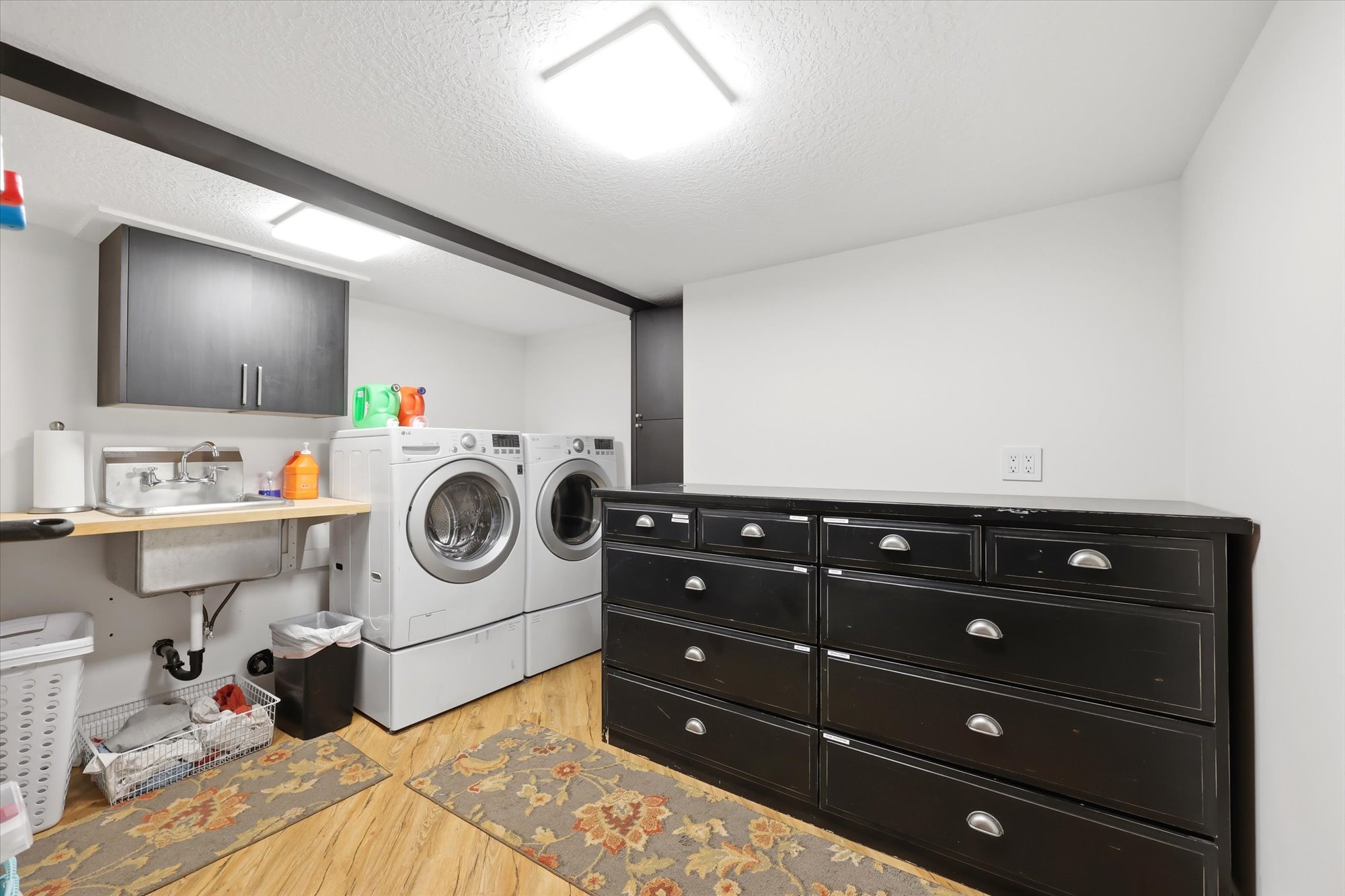 Laundry area featuring cabinet space, a textured ceiling, light wood-style flooring, and independent washer and dryer