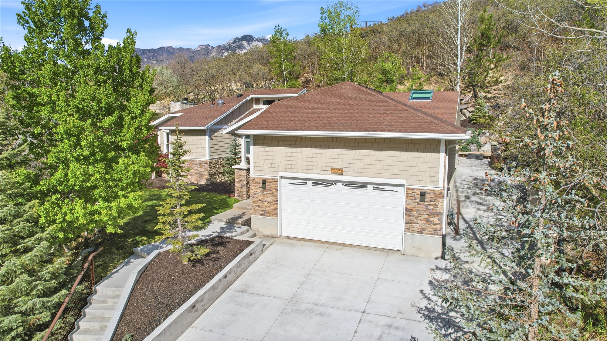 View of front of home featuring stone siding, a garage, concrete driveway, a shingled roof, and a mountain view