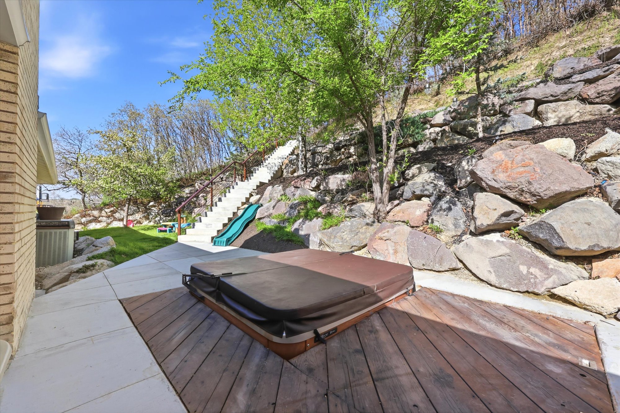 Wooden deck with a playground, a covered hot tub, and a patio area
