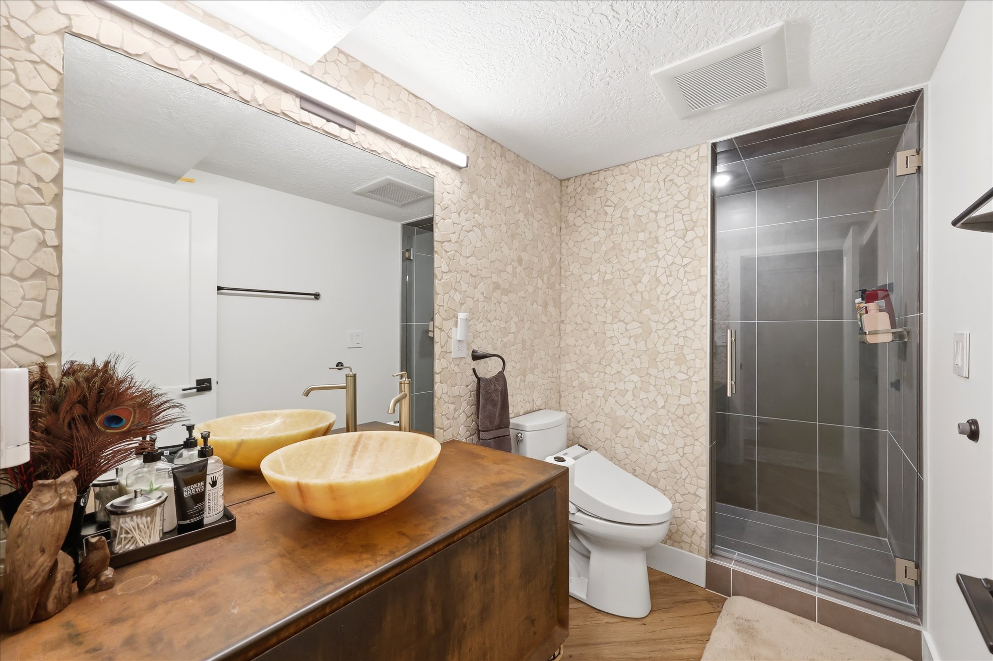 Full bath featuring a textured ceiling, vanity, a stall shower, wallpapered walls, and light wood-style floors