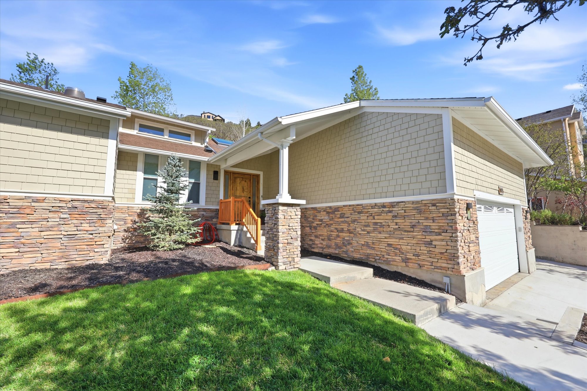 View of front of property featuring stone siding, a front yard, concrete driveway, and a garage