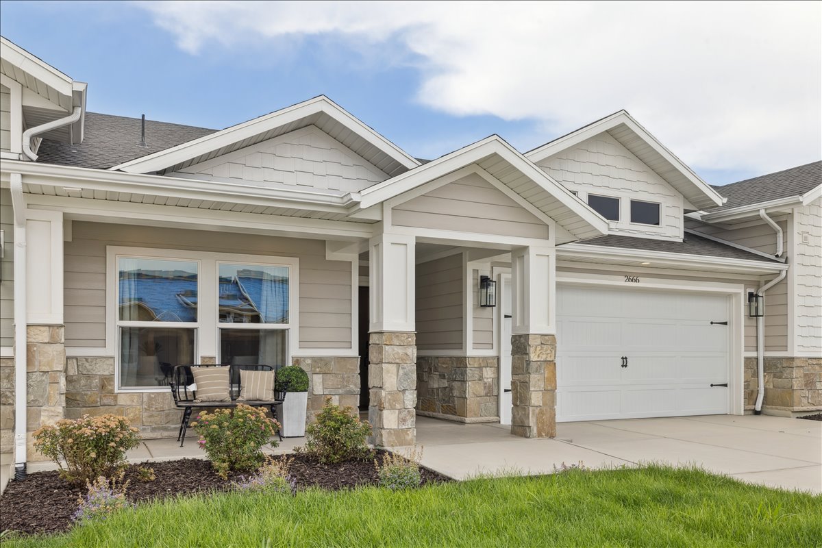 Craftsman-style home featuring stone siding, a porch, a shingled roof, a garage, and concrete driveway