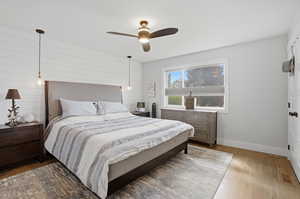 Bedroom with wood finished floors, a ceiling fan, and wooden walls