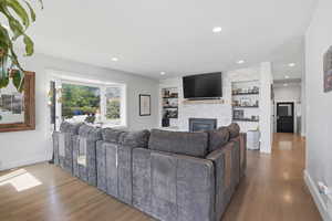 Living area featuring wood finished floors, a stone fireplace, built in shelves, and recessed lighting