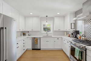 Kitchen with stainless steel appliances, white cabinets, light wood-style floors, decorative light fixtures, and backsplash