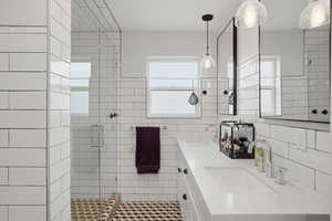 Full bath with double vanity, a shower stall, and tile walls