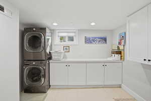 Laundry room featuring cabinet space, stacked washer and dryer, and recessed lighting