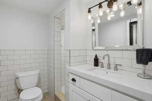 Full bathroom featuring vanity, tile walls, a shower, and wainscoting