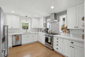 Kitchen featuring white cabinets, stainless steel appliances, light wood-style flooring, pendant lighting, and light stone countertops