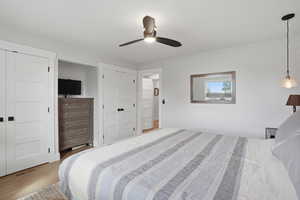 Bedroom with light wood-style flooring, ceiling fan, and multiple closets