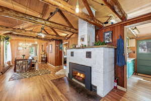 Living area with light wood-style floors, a tile fireplace, plenty of natural light, vaulted ceiling with beams, and wooden walls