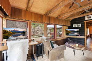 Living area featuring radiator heating unit, wood finished floors, and vaulted ceiling with beams