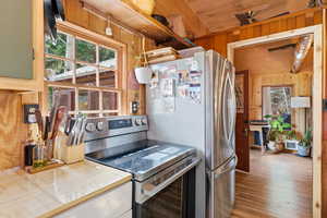 Kitchen featuring stainless steel range with electric cooktop, wood walls, tile countertops, and wood finished floors