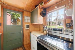 Kitchen with stainless steel range with electric stovetop, tile countertops, wooden walls, dark wood-style floors, and white cabinetry