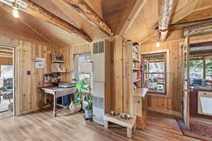 Office space featuring plenty of natural light, lofted ceiling with beams, a heating unit, light wood-style flooring, and wood walls