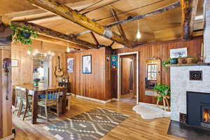 Dining space featuring vaulted ceiling with beams, wooden walls, suspended lighting, a fireplace, and wood finished floors