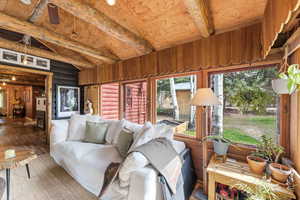 Living area with log walls, beam ceiling, hardwood / wood-style floors, and a ceiling fan