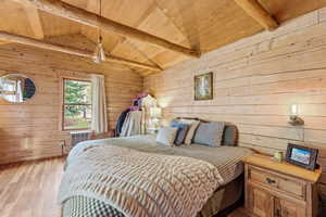 Bedroom featuring wood walls, wood finished floors, a wood ceiling with exposed beams, and ceiling fan