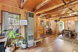 Living room with wooden walls, a heating unit, light wood-style flooring, beam ceiling, and hanging lights