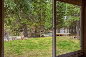 View of green lawn with a water view, a sunroom, and view of wooded area
