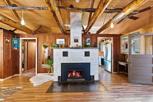 Detailed view of beam ceiling, wooden walls, freestanding refrigerator, wood finished floors, and a tiled fireplace