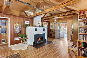 Living area featuring wood walls, wood finished floors, a tiled fireplace, heating unit, and a wooden ceiling with exposed beams