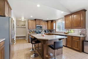 Kitchen featuring stainless steel appliances, a breakfast bar, wood finish cabinets, light countertops, and recessed lighting