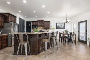 Kitchen featuring dark wood finish cabinetry, light stone counters, a kitchen bar, stainless steel appliances, and a large island