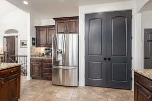 Kitchen with dark wood finish cabinets, light stone countertops, and stainless steel refrigerator with ice dispenser