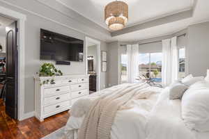 Bedroom with dark wood-style floors, ensuite bathroom, a tray ceiling, access to exterior, and suspended lighting