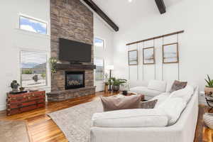 Living area with wood-type flooring, a stone fireplace, and lofted ceiling
