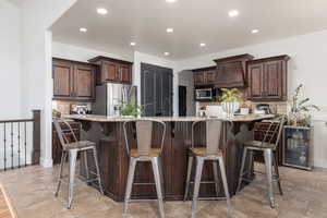 Kitchen with dark wood finish cabinets, light stone counters, a kitchen bar, decorative backsplash, and beverage cooler