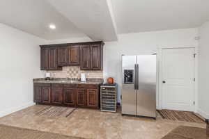 Kitchen with dark wood finish cabinetry, stainless steel refrigerator with ice dispenser, beverage cooler, and tasteful backsplash