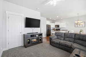 Living room with a ceiling fan, a chandelier, dark colored carpet, and a glass covered fireplace